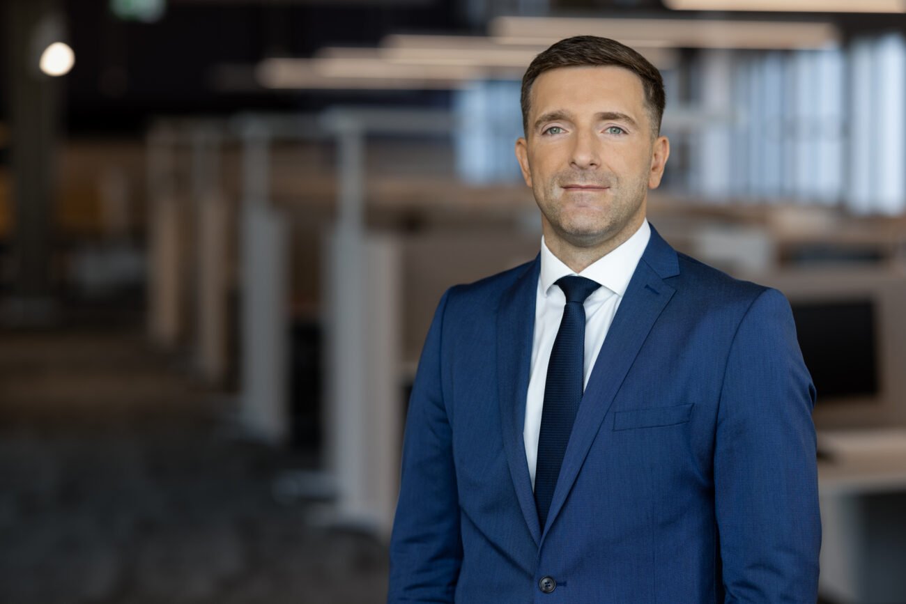 Mėlynu kostiumu pasipuošęs vyras stovi moderniame biure
