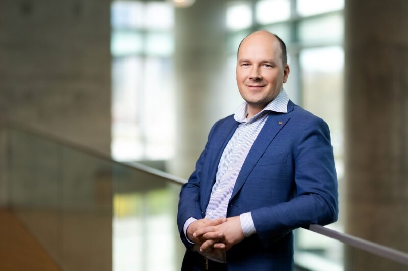 Besišypsantis vyras su mėlynu švarku pozuoja moderniame pastate