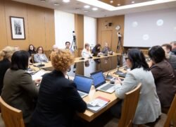 Dalyviai susėdę prie stalo diskutuoja konferencijų salėje