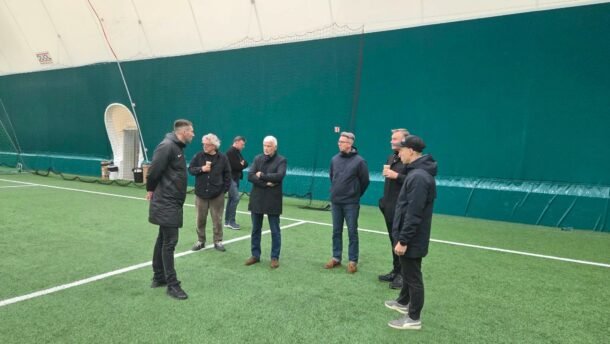 Žmonių grupė kalbasi uždarame futbolo manieže ant dirbtinės dangos