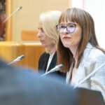Dvi moterys posėdžių salėje sėdi prie mikrofonų