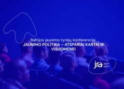 Mėlyna šviesa apšviesti konferencijos dalyviai sėdi auditorijoje