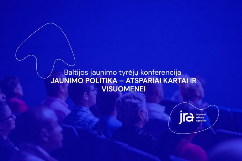 Mėlyna šviesa apšviesti konferencijos dalyviai sėdi auditorijoje