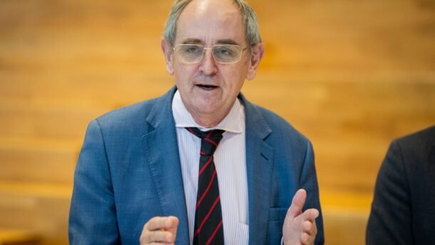 Akinius dėvintis vyras su kostiumu kalba ir gestikuliuoja