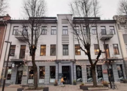Kauno gatvėje esančio pastato fasadas su vitrinomis ir lauko girliandomis