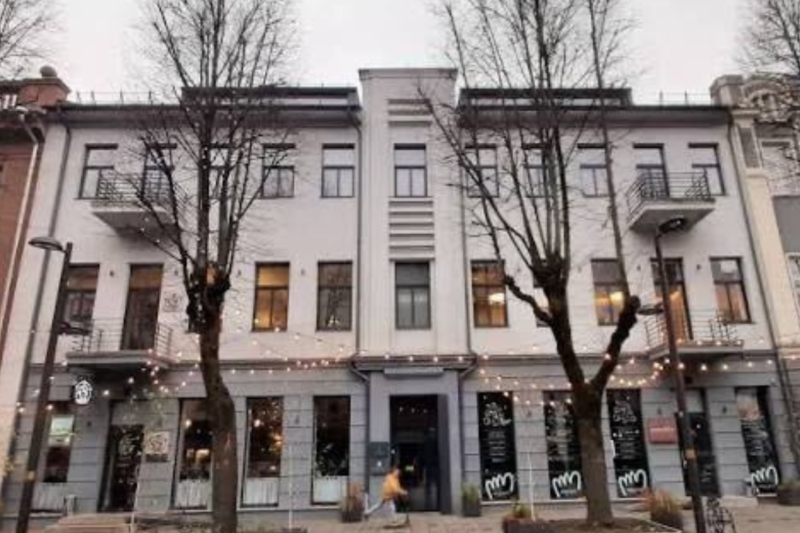 Kauno gatvėje esančio pastato fasadas su vitrinomis ir lauko girliandomis