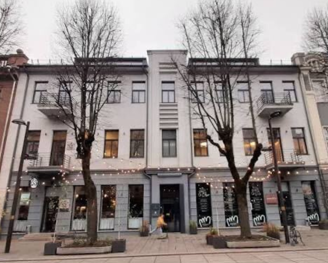 Kauno gatvėje esančio pastato fasadas su vitrinomis ir lauko girliandomis