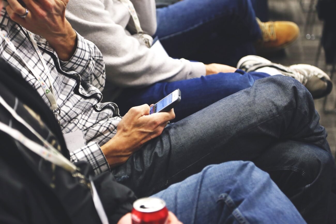 Sėdintis žmogus laiko išmanųjį telefoną, o šalia matomi kiti keleiviai