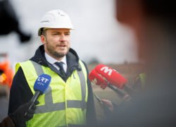 Statybos sektoriaus atstovas su šalmu ir liemene kalba žurnalistams