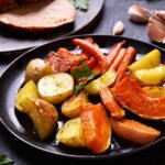 Keptos bulvės, morkos, moliūgas ir paprika juodoje lėkštėje