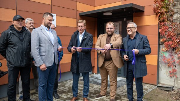 Vyrai prie pastato įėjimo laiko violetinę juostelę atidarymo ceremonijoje