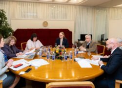 Komisijos posėdžio dalyviai sėdi prie stalo su dokumentais
