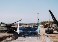 Tankas statybvietėje šalia ekskavatorių, krano ir informacinio stendo