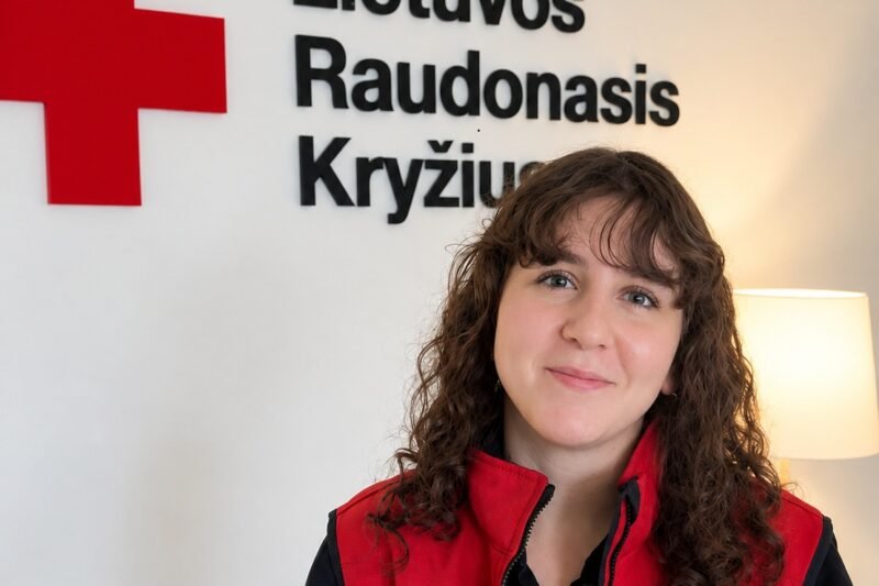 Moteris su Lietuvos Raudonojo Kryžiaus liemene prie organizacijos logotipo