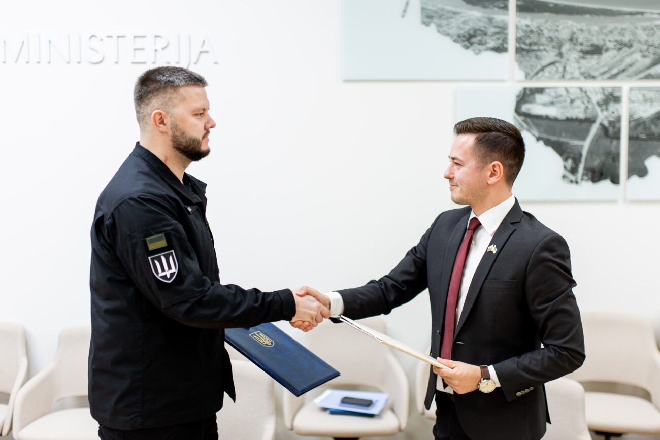 Uniformuotas vyras ir vyras su kostiumu spaudžia vienas kitam rankas