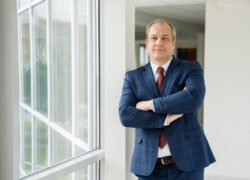 Verslo vyras su kostiumu stovi sukryžiavęs rankas prie lango