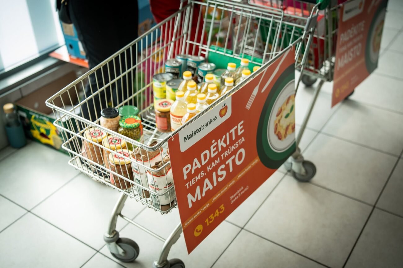 Prekių vežimėlis su maisto produktais ir „Maisto banko“ akcijos plakatu