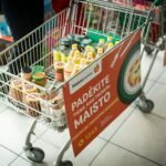 Prekių vežimėlis su maisto produktais ir „Maisto banko“ akcijos plakatu