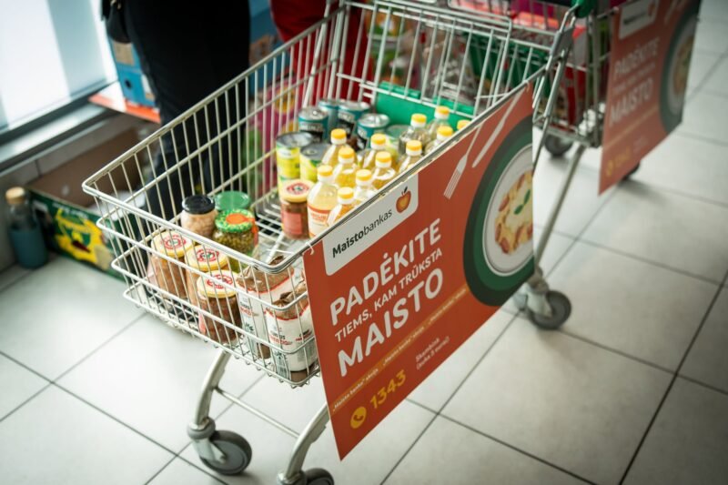 Prekių vežimėlis su maisto produktais ir „Maisto banko“ akcijos plakatu