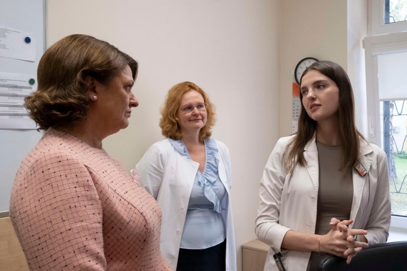 Trys moterys medicinos įstaigos patalpoje, dvi vilki baltus chalatus