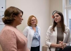 Trys moterys medicinos įstaigos patalpoje, dvi vilki baltus chalatus