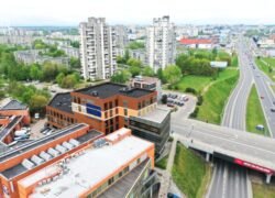 Aukštai fotografuotas miesto vaizdas su verslo pastatu, daugiabučiais ir kelių sankryža