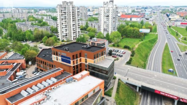 Aukštai fotografuotas miesto vaizdas su verslo pastatu, daugiabučiais ir kelių sankryža