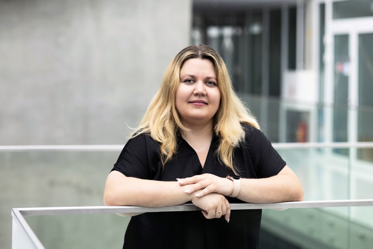 Moteris juodais marškiniais stovi prie stiklinio turėklo moderniame pastate
