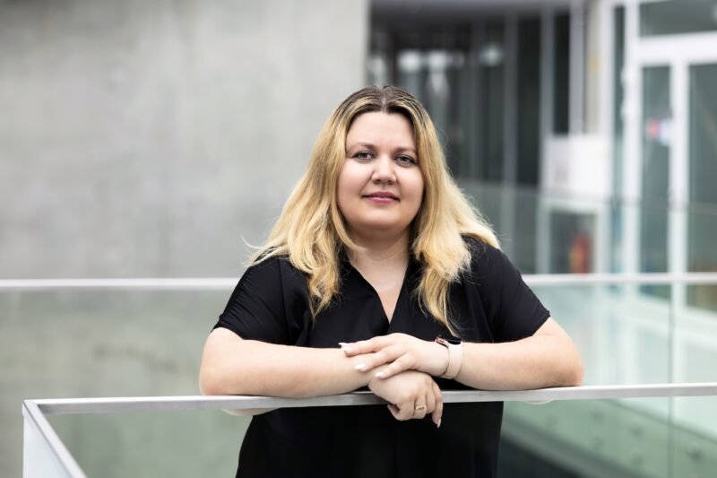 Moteris juodais marškiniais stovi prie stiklinio turėklo moderniame pastate