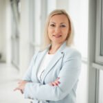 Besijuokianti moteris šviesiame biure, sukryžiavusi rankas