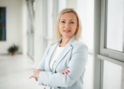 Besijuokianti moteris šviesiame biure, sukryžiavusi rankas