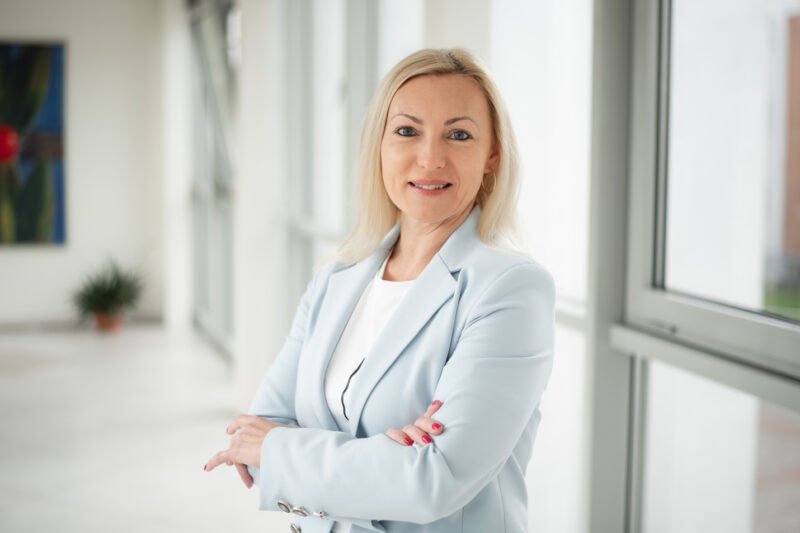 Besijuokianti moteris šviesiame biure, sukryžiavusi rankas