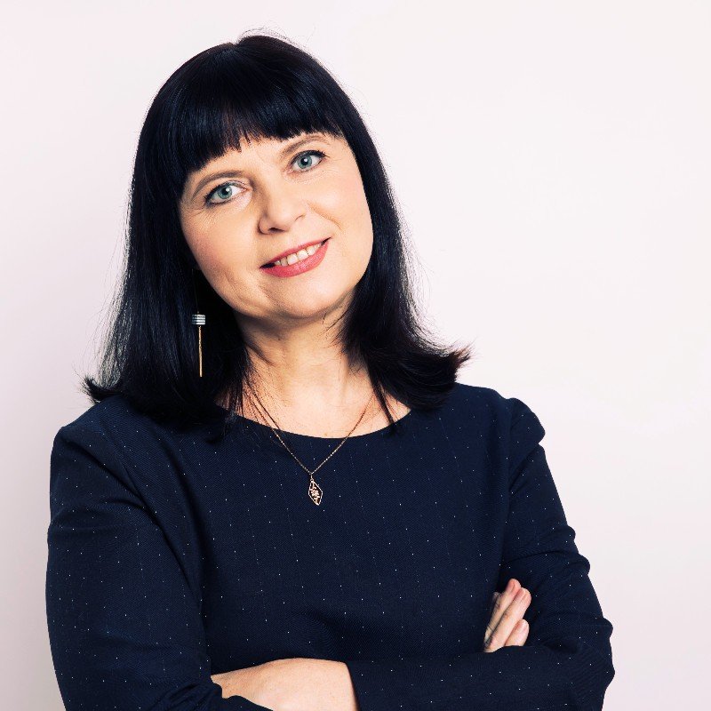Besijuokianti moteris juodais plaukais ir tamsia palaidine sukryžiuotomis rankomis