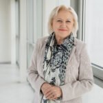 Besišypsanti žilaplaukė moteris su raštuotu šaliku šviesiame koridoriuje