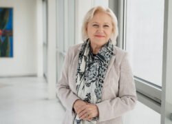 Besišypsanti žilaplaukė moteris su raštuotu šaliku šviesiame koridoriuje