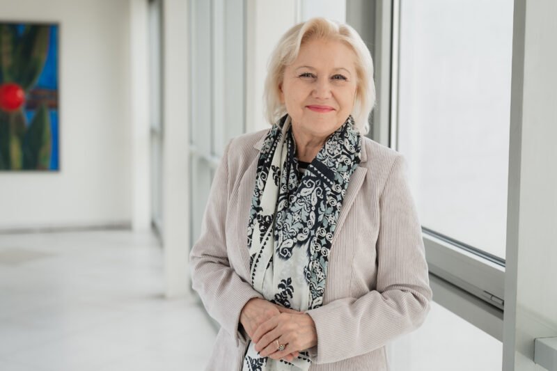 Besišypsanti žilaplaukė moteris su raštuotu šaliku šviesiame koridoriuje