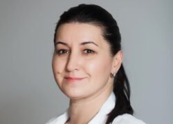 Besidominti moteris baltais drabužiais žvelgia į fotoaparatą