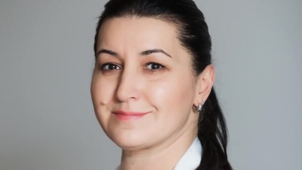 Besidominti moteris baltais drabužiais žvelgia į fotoaparatą