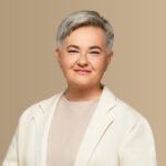 Besijuokianti trumpaplaukė moteris šviesiu švarku neutraliame fone