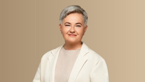 Besijuokianti trumpaplaukė moteris šviesiu švarku neutraliame fone