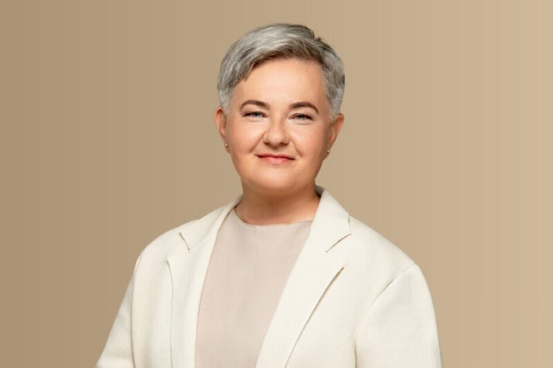 Besijuokianti trumpaplaukė moteris šviesiu švarku neutraliame fone