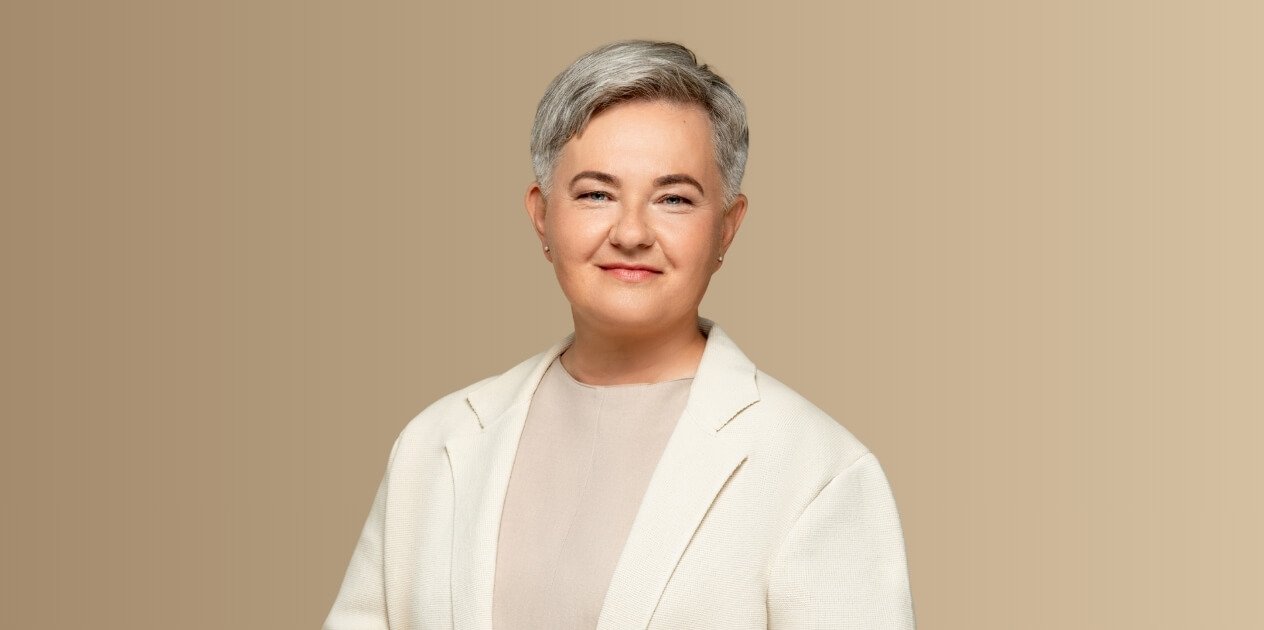Besijuokianti trumpaplaukė moteris šviesiu švarku neutraliame fone
