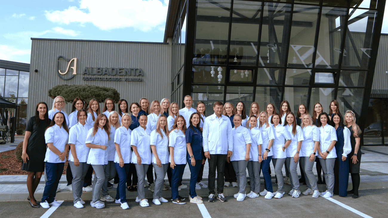 Odontologijos klinikos darbuotojų grupė pozuoja prie modernaus pastato