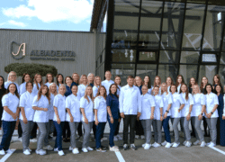 Odontologijos klinikos darbuotojų grupė pozuoja prie modernaus pastato