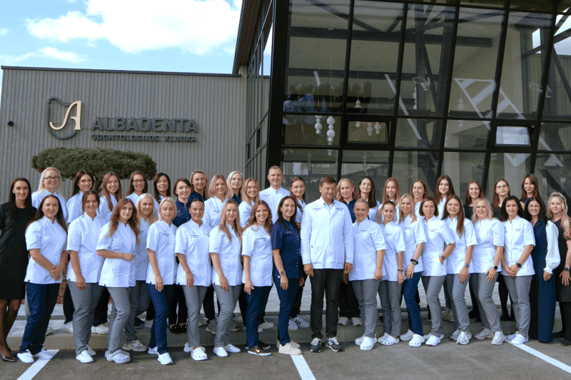 Odontologijos klinikos darbuotojų grupė pozuoja prie modernaus pastato