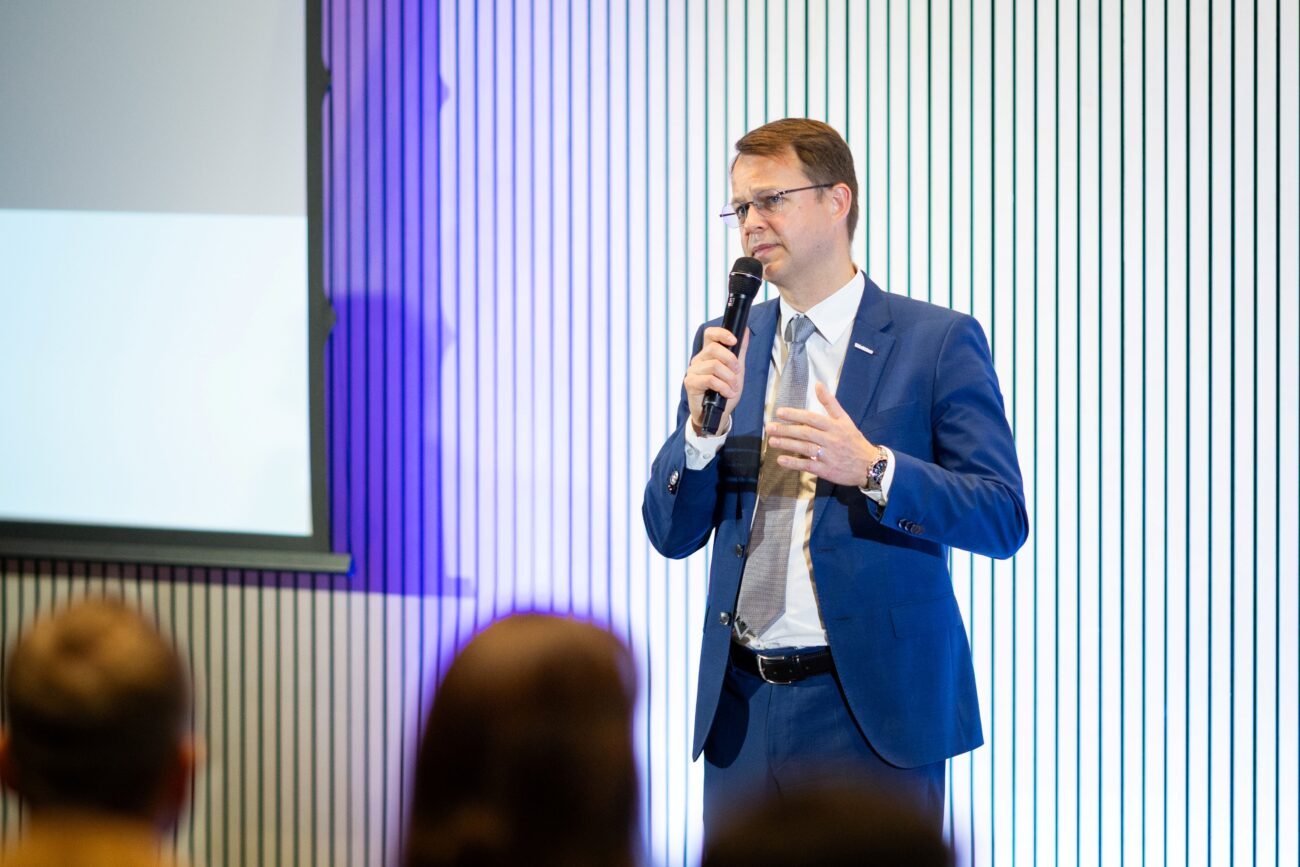 Verslo kostiumu vilkintis vyras kalba į mikrofoną priešais auditoriją