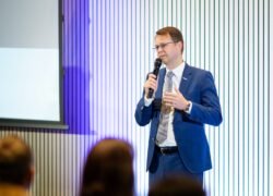 Verslo kostiumu vilkintis vyras kalba į mikrofoną priešais auditoriją