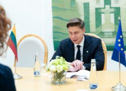 Premjeras sėdi prie stalo šalia Lietuvos ir Europos Sąjungos vėliavų