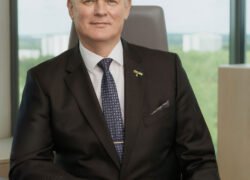 Vyras su kostiumu sėdi prie darbo stalo biuro aplinkoje