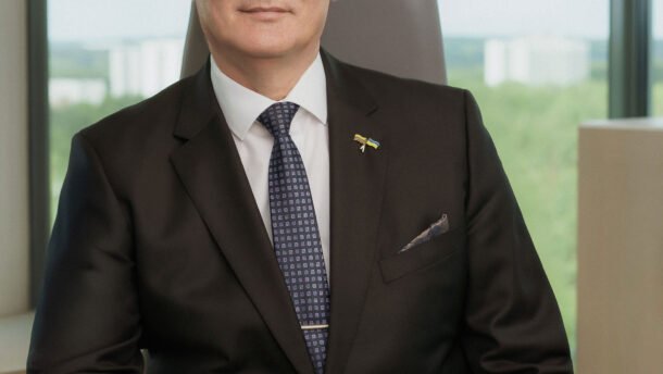 Vyras su kostiumu sėdi prie darbo stalo biuro aplinkoje